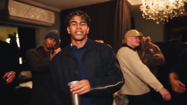 A smiling guest in a dark jacket dances and waves with friends.