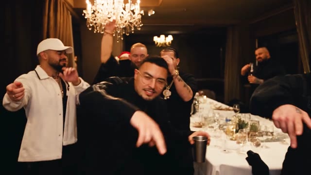A guest wearing glasses holds a metal cup while celebrating with friends.